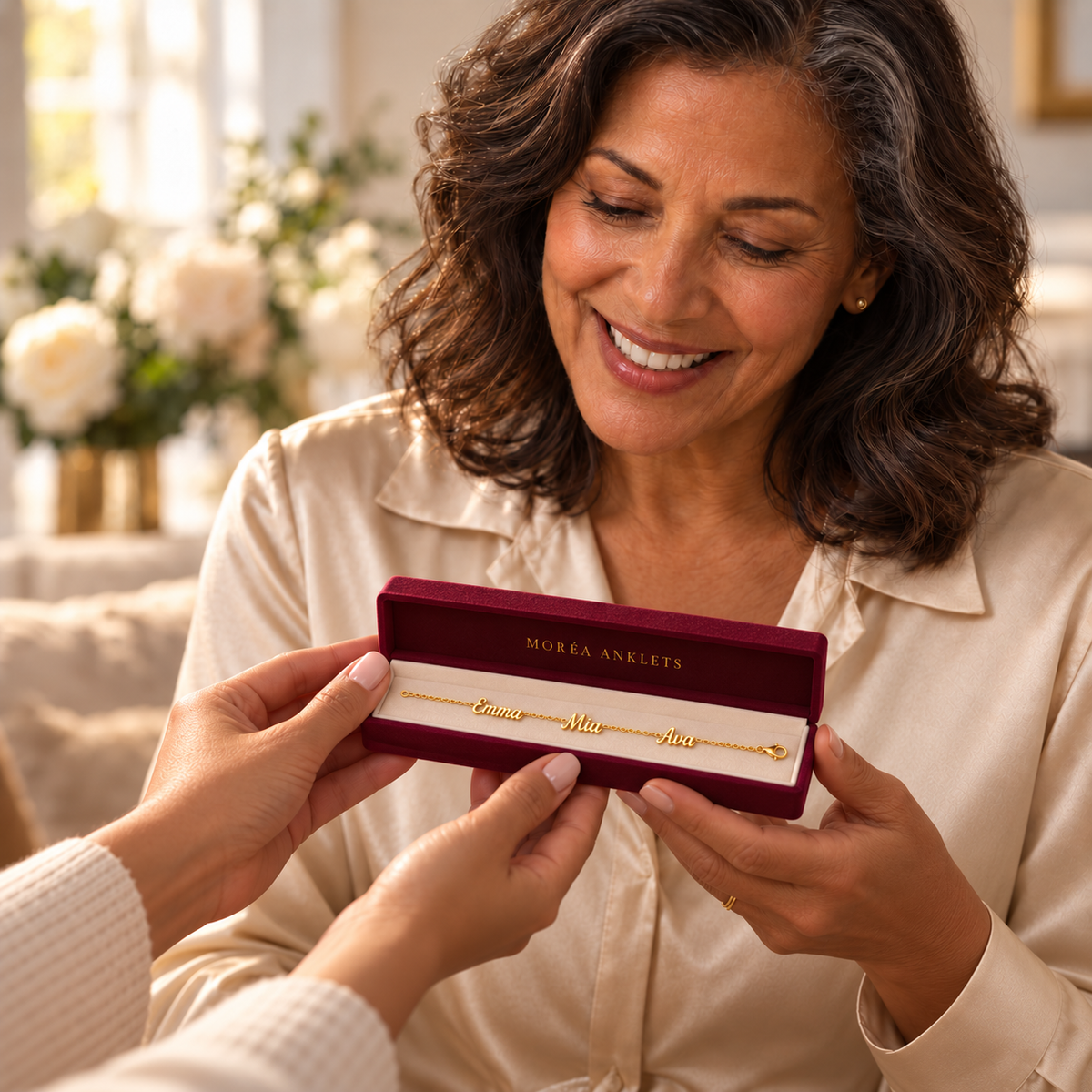 A mother receiving a personalized gold name anklet in a compact rectangular burgundy Moréa Anklets gift box